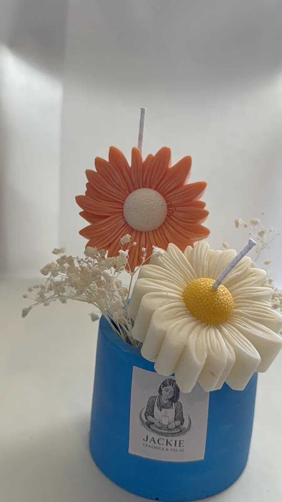 Velas artesanales en forma de margarita en una maceta azul con flores secas
